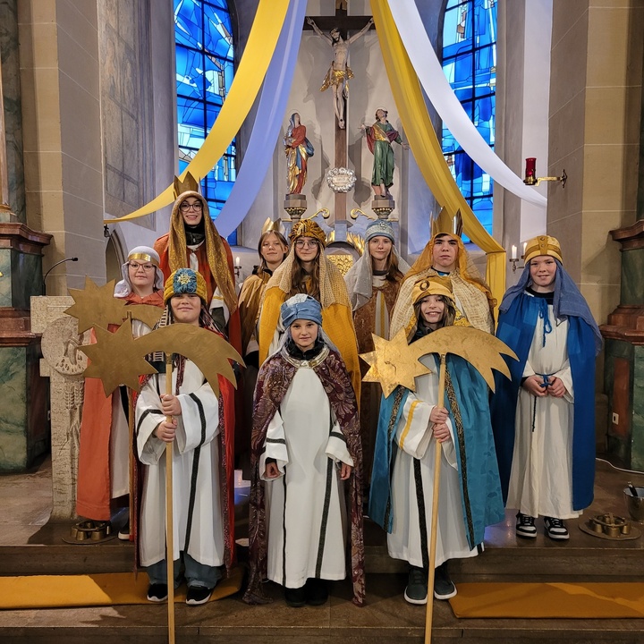 Zehn Kinder stehen als Sternsinger verkleidet vor dem Altar und schauen in die Kamera