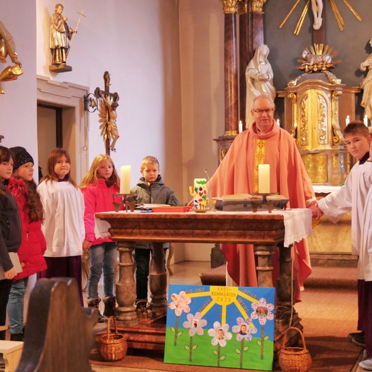 Pfarrer Rügamer und die Kinder stehen um den Altar und fassen sich an den Händen
