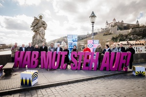 Auf der Mainbrücke stehen Menschen hinter dem Schriftzug "Hab Mut Steh Auf". Im Hintergrund ist die Festung Marienberg zu sehen.