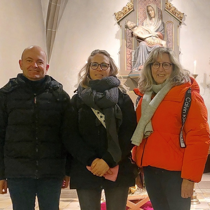 Drei Personen stehen im Altarraum und schauen in die Kamera.